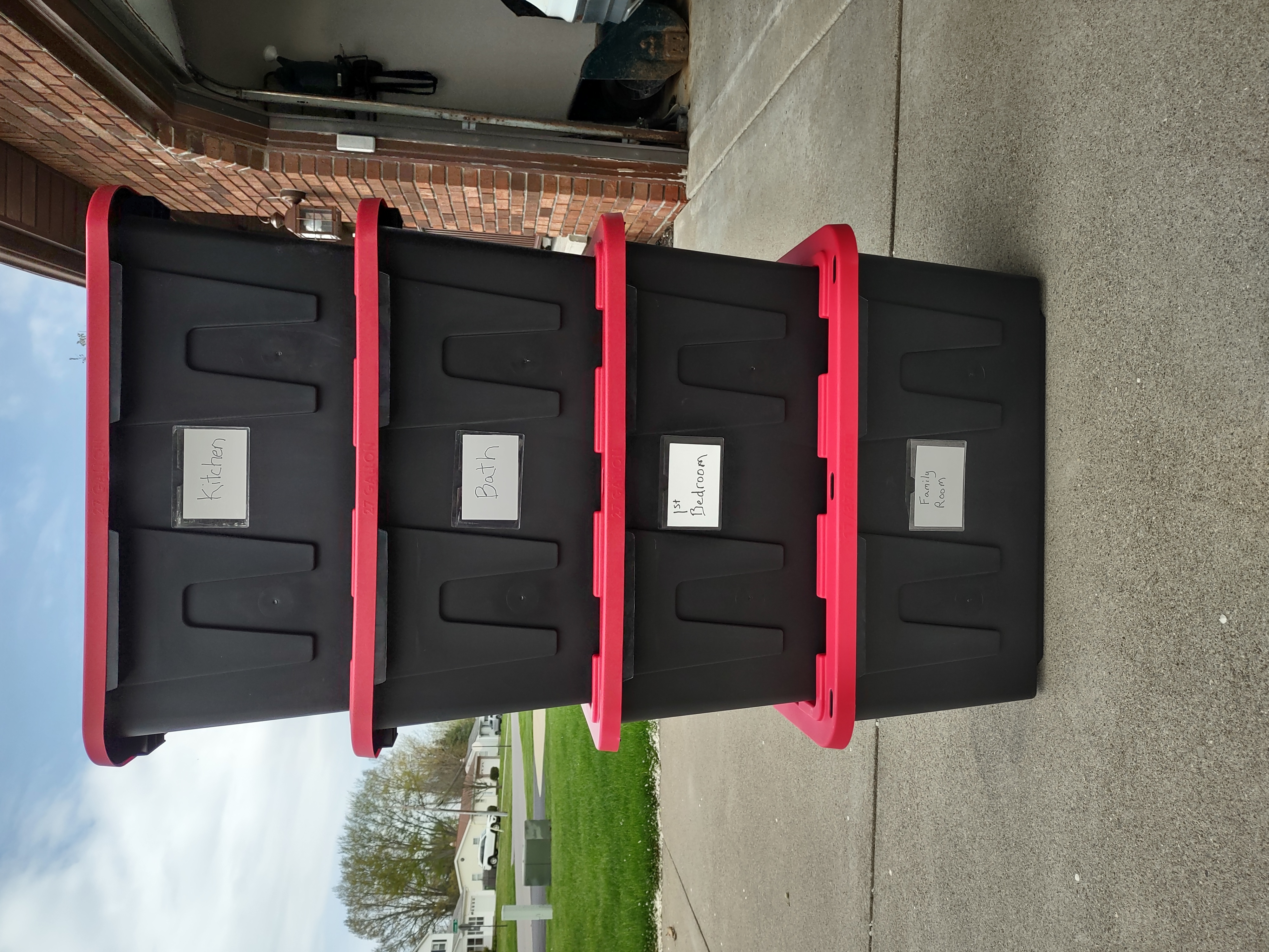 Stack of reusable black and red moving totes with room labels including Kitchen, Bath, Bedroom and Family Room